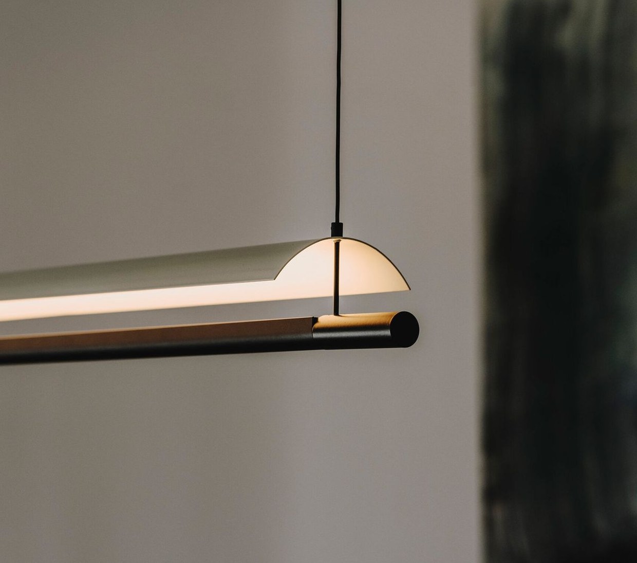 Langwerpige hanglamp boven een werkplek tegen een lichte wand