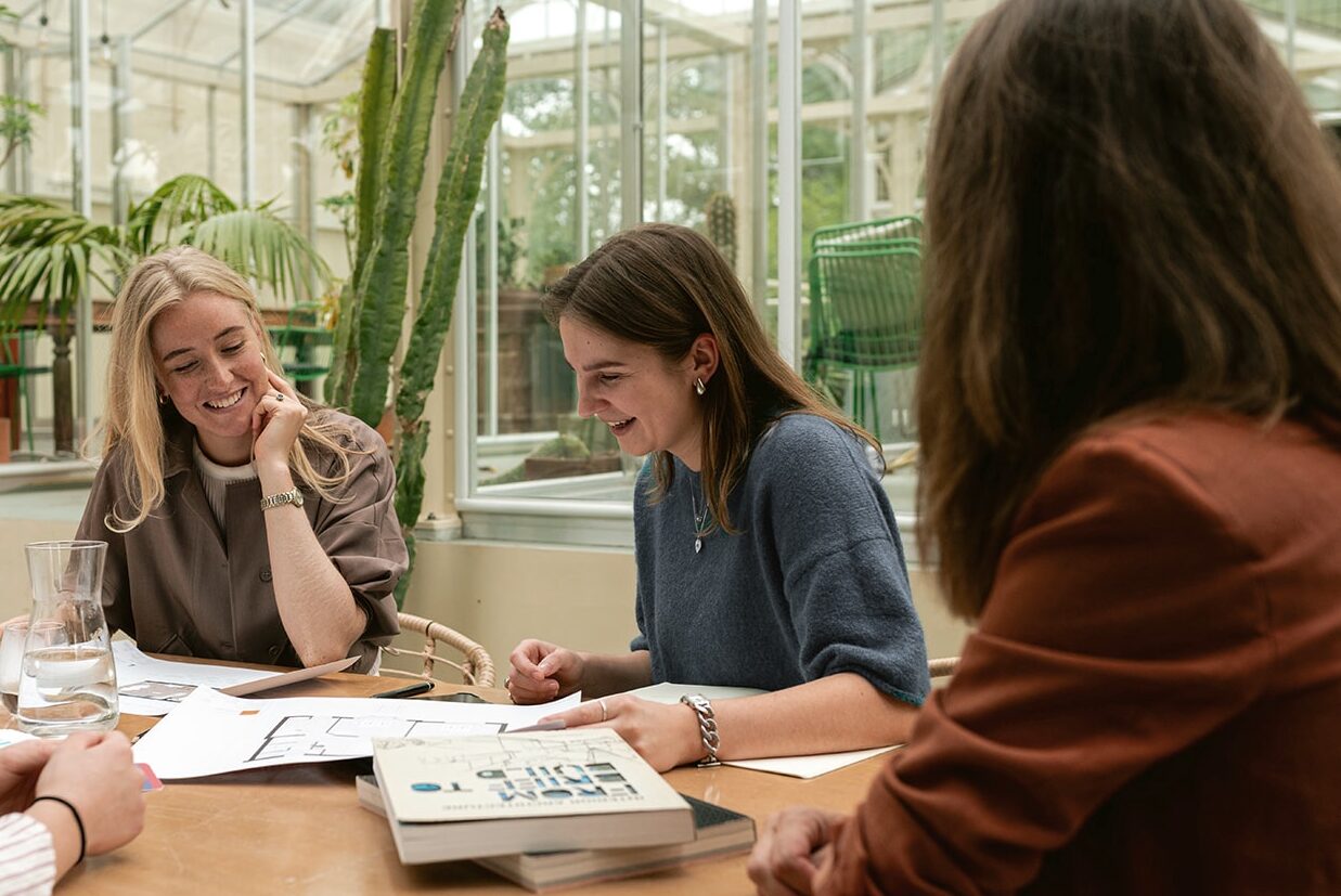 Vier collega’s bespreken een ontwerp aan tafel in een lichte serre